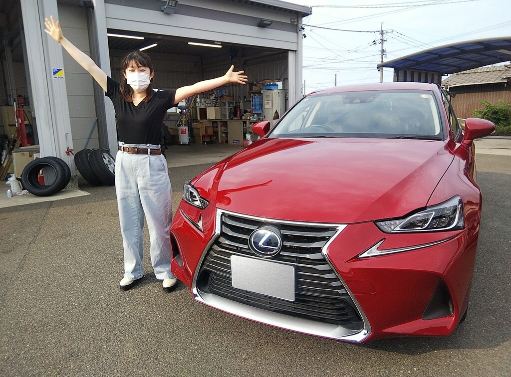 画像：赤い車の横に手を広げて立つ女性